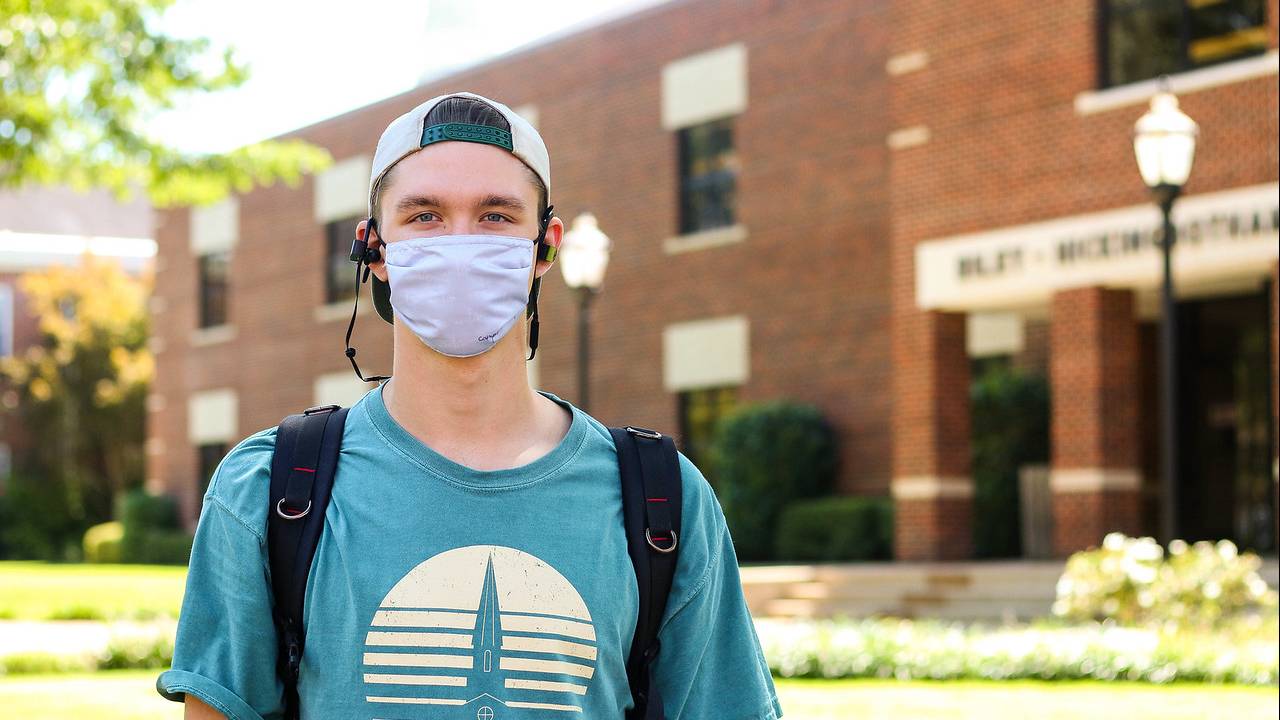 Student wearing mask stands in front of Ouachita's Riley-Hickingbotham Library