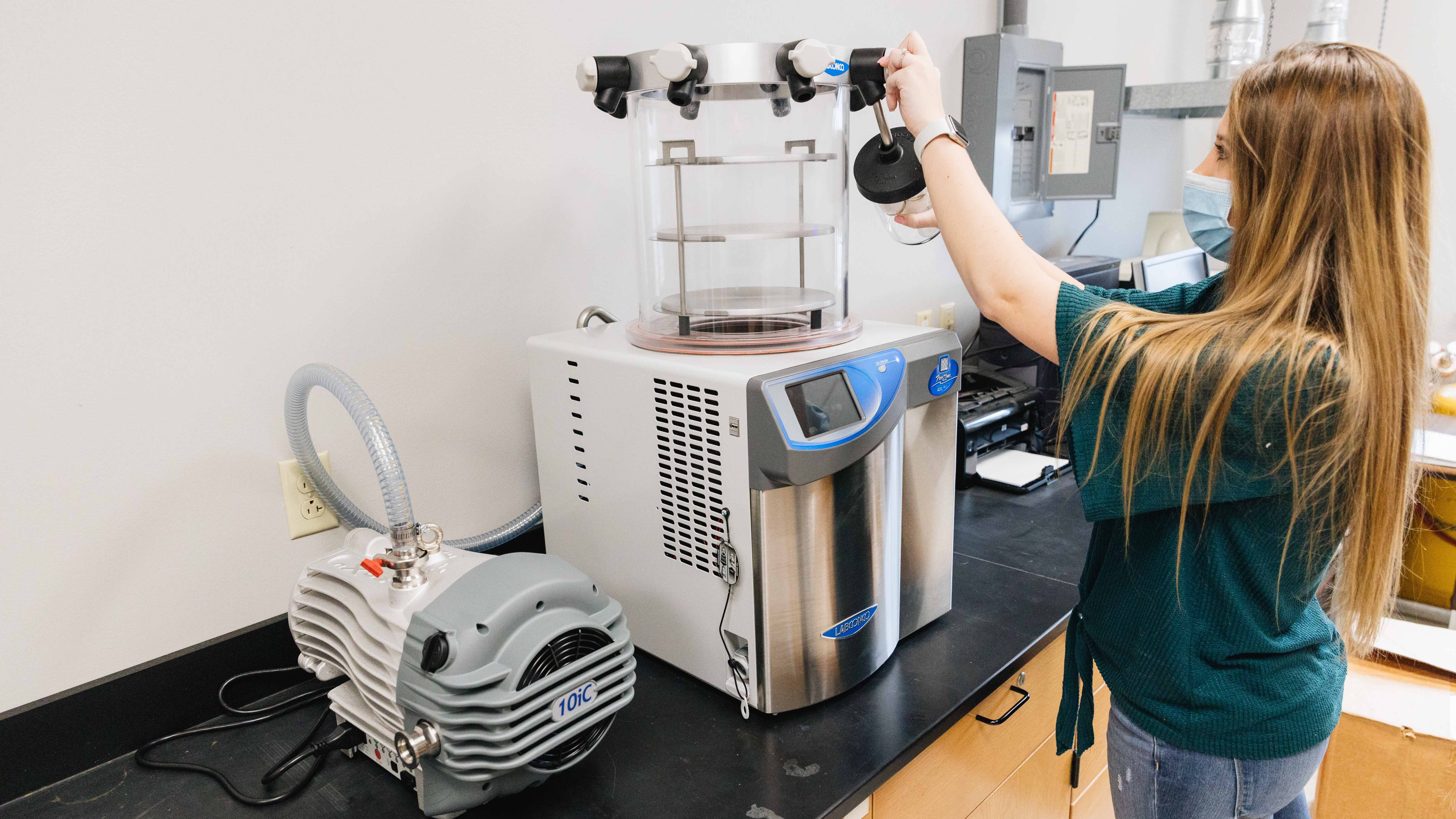 Student poses with School of Natural Sciences' new lyophilizer